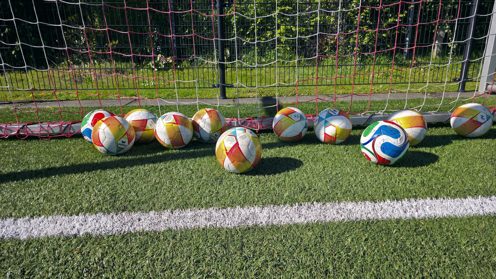 Bunte Trainingsbälle liegen am Tor auf dem Kunstrasen