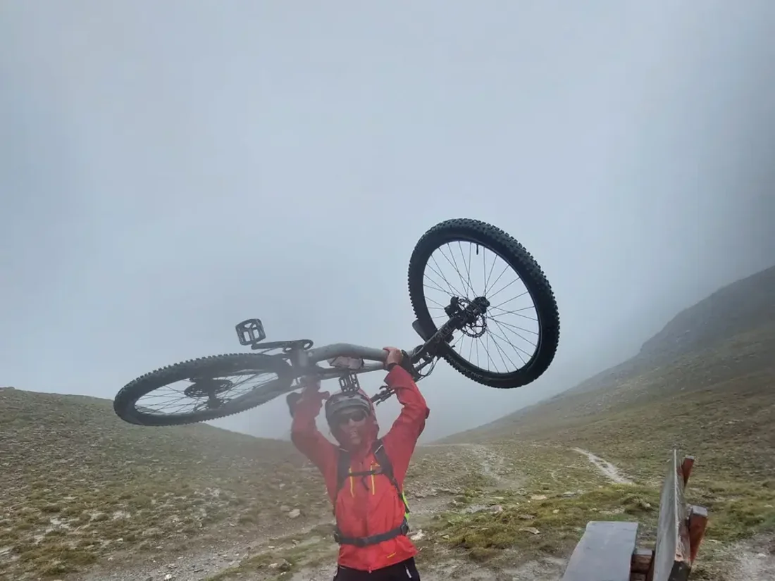Mountainbiker hält sein Rad in dichtem Nebel über den Kopf, Blick auf einen Bergpfad